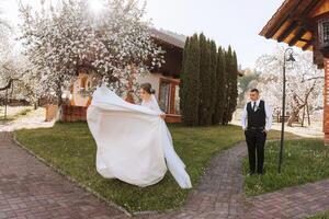 das Braut ist kreisen im ihr Hochzeit Kleid, und das Bräutigam ist suchen beim ihr. Hochzeit Foto Session im ein schön Frühling Park.