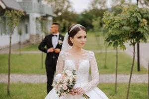 ein schön jung Braut, im ein Sommer- Park, Spaziergänge voraus von ihr Bräutigam. schön Hochzeit Weiß Kleid. Spaziergänge im das Park. ein glücklich und liebend Paar. foto