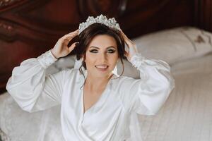 ein schön Brünette Braut mit ein Tiara im ihr Haar ist bekommen bereit zum das Hochzeit im ein schön Kleid im Boudoir Stil. Nahansicht Hochzeit Porträt, Foto. foto