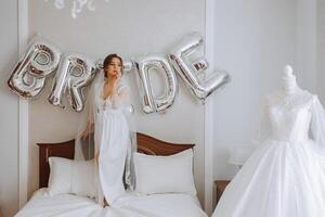 Luftballons Braut und ein schön Braut Sitzung auf ein Bett im ein luxuriös Boudoir Kleid vorbereiten zum das Hochzeit Zeremonie. foto