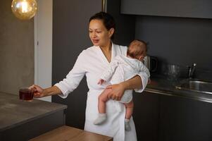 Mama Getränke Tee und trägt Baby Junge beim Zuhause foto