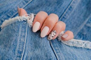 schön weiblich Hände mit Maniküre auf das Hintergrund von Denim. stilvoll Nagel Design. Herbst Maniküre mit Beige Farbe und Leopard Muster auf das Nägel. foto