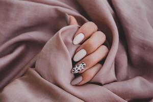 Frau Hand mit ein schön oval geformt Maniküre. Herbst Trend, Beige Farbe Polieren mit Leopard Muster auf Nägel mit Gel Polieren, Schellack. foto