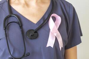 Schuss von das weiblich Arzt gegen das Weiß Mauer mit Rosa Band, wie ein Symbol von ein Brust Krebs Bewusstsein. Konzept foto