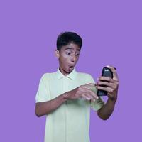 jung asiatisch Mann überrascht suchen beim Clever Telefon, tragen Gelb T-Shirt, isoliert lila Hintergrund. foto