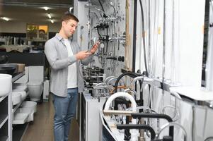 Mann wählt ein Badezimmer Wasserhahn im ein Konstruktion Supermarkt, Installation Instandsetzung im das Haus foto