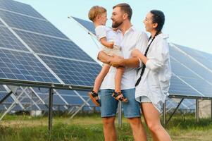 jung Familie mit ein klein Kind im ihr Waffen auf ein Hintergrund von Solar- Tafeln. ein Mann und ein Frau aussehen beim jeder andere mit Liebe. Solar- Energie Konzept. foto