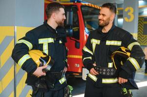 zwei Feuerwehrleute im schützend Kleidung im Helme mit Feuer Motor foto