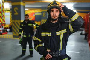 Porträt von zwei jung Feuerwehrmänner im Uniform Stehen Innerhalb das Feuer Bahnhof foto