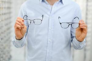 Mann wählt Brille zum Vision Korrektur im ein Augenheilkunde Salon. Brille zum Vision Korrektur foto