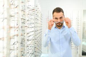 Mann wählt Brille zum Vision Korrektur im ein Augenheilkunde Salon. Brille zum Vision Korrektur foto