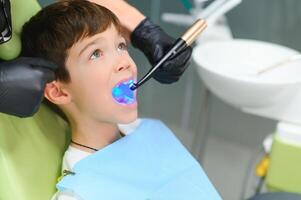 ein wenig Junge haben seine Zahn erledigt im das Klinik - - Putten das Photopolymer Lampe mit Blau Licht im das Mund foto