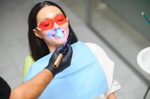 Zahnarzt Aushärten das Patienten Zähne mit ultraviolett Lampe im seine Büro foto