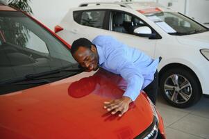 Neu Auto Eigentümer. glücklich afrikanisch amerikanisch Mann berühren umarmen seine Brandneu Auto foto