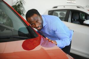 Neu Auto Eigentümer. glücklich afrikanisch amerikanisch Mann berühren umarmen seine Brandneu Auto foto