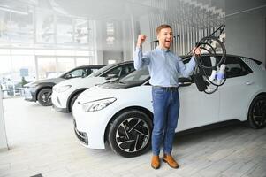 Bart Mann versuchen ein Neu Laden Kabel mit ein Auto Laden Bahnhof beim das Motor- Händler. Konzept von Kauf elektrisch Fahrzeug. Clever ökologisch Leben foto