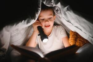 Porträt von süß wenig Junge lesen im Bett mit Taschenlampe im dunkel Zimmer, genießen Märchen foto