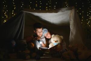 lesen und Familie Spiele im Kinder- Zelt. Junge und Mädchen mit Buch und Taschenlampe Vor gehen zu Bett. foto