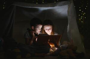 lesen und Familie Spiele im Kinder- Zelt. Junge und Mädchen mit Buch und Taschenlampe Vor gehen zu Bett. foto