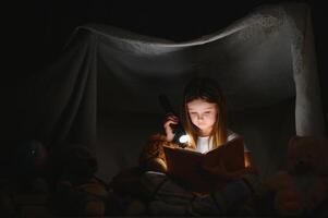 ein ziemlich wenig Mädchen lesen ein Buch auf das Fußboden unter das Lampe. Kinder und Bildung foto