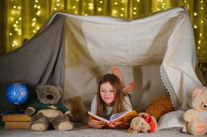 Kind Mädchen lesen mit Buch und Taschenlampe und Teddy Bär im Zelt. Vor gehen zu Bett. foto