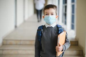 wenig Schüler tragen Maske während Corona Virus und Grippe Ausbruch. Krankheit Schutz zum Kinder. Maske zum Coronavirus Verhütung. Schule Kind Husten. wenig Junge atmet durch Maske, gehen zu Schule foto