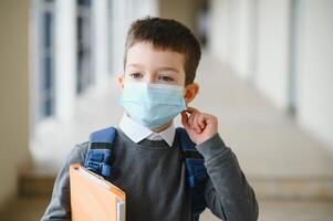 wenig Schüler tragen Maske während Corona Virus und Grippe Ausbruch. Krankheit Schutz zum Kinder. Maske zum Coronavirus Verhütung. Schule Kind Husten. wenig Junge atmet durch Maske, gehen zu Schule. foto