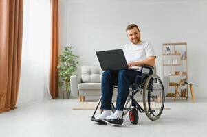 Arbeit beim heim. gelähmt männlich Person halten Laptop auf Knie und behalten Lächeln auf Gesicht während suchen beim Bildschirm foto