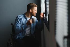 zurück Aussicht von Geschäftsmann im Rollstuhl Sitzung im Büro und aussehen durch Fenster. foto