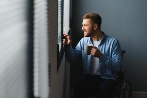 zurück Aussicht von Geschäftsmann im Rollstuhl Sitzung im Büro und aussehen durch Fenster. foto