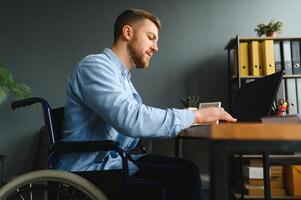 deaktiviert Person im das Rollstuhl funktioniert im das Büro beim das Computer. er ist lächelnd und leidenschaftlich Über das Arbeitsablauf foto