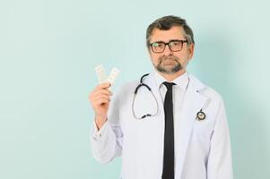 zuversichtlich männlich Arzt im Weiß medizinisch Jacke halten Tabletten während suchen beim das Kamera isoliert auf Blau Hintergrund. Medizin Konzept. foto