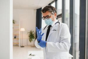 Fachmann Arzt im medizinisch Maske Putten auf Handschuhe. zuversichtlich Arzt im Labor Mantel tragen Schutz während covid-19 Ausbruch. Verhütung von viral Krankheiten. foto