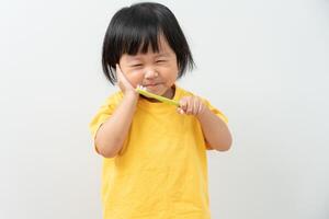 wenig asiatisch Mädchen drückt Hand zu Wange, leidet von Schmerzen im Zahn. Zähne Verfall, Dental Probleme, Kind Emotionen und Gesichts- Ausdruck, Oral Gesundheit Pflege, reduzieren Süßigkeiten, Fluor Glasur foto