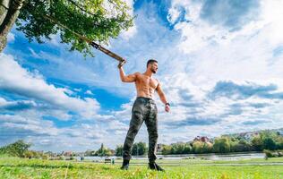 ein stark Mann mit ein Baseball Schläger. ein mit nacktem Oberkörper Mann halten ein Baseball Schläger im ein Park foto