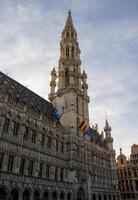 ikonisch Turm von das Brüssel Stadt, Dorf Halle unter ein wolkig Himmel, geschmückt mit Belgier und EU Flaggen - - ein gotisch Wunder foto