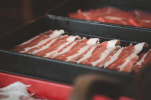 roh frisch dünn Rindfleisch im schwarz Tablett bereit zum Sukiyaki foto