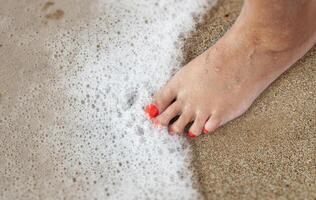 Damen Füße mit ein Pediküre im das Sand auf das Strand foto