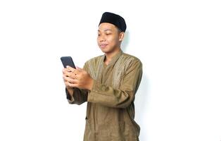 Seite Aussicht von zufrieden asiatisch Muslim Mann lesen ein Botschaft mit Handy, Mobiltelefon Telefon isoliert auf Weiß Hintergrund foto