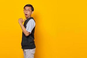 hübscher asiatischer mann überrascht und zeigt auf leeren raum isoliert auf gelbem hintergrund foto