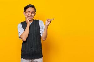 Porträt eines fröhlichen jungen asiatischen Mannes, der mit dem Finger auf den leeren Raum zeigt, isoliert auf gelbem Hintergrund foto