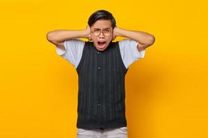Frustrierter asiatischer junger Mann, der die Ohren mit den Händen bedeckt, die auf gelbem Hintergrund isoliert sind foto
