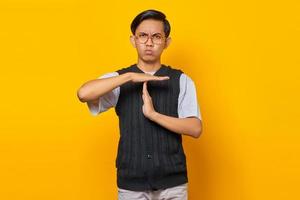 Porträt des jungen asiatischen Mannes, der Timeout-Geste auf gelbem Hintergrund zeigt