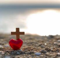 ai generiert rot Herz mit hölzern Christian Kreuz auf Kies Fußboden im Morgen Licht foto