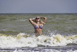 schön blond Stehen im Meer Wasser. Mädchen mit Sonnenbrille auf foto