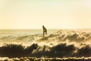 ein unbekannt Surfer Fahrten ein groß Welle mit Schaum beim Sonnenuntergang foto