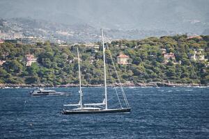 Monaco, Mega Yacht und enorm segeln Boot sind im Meer beim sonnig Tag, Insel ist nahe, enorm Motor- Boot, Reichtum Leben von Milliardäre, Berge auf Hintergrund foto