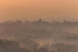 Silhouette von das Borobudur Tempel auf ein neblig Morgen, das golden Farbe von Morgen Licht umgibt das Tempel, Indonesien foto