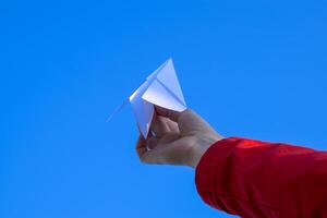 Weiß Papier Flugzeug im Hand gegen das Himmel. ein Symbol von Freiheit auf das Internet foto