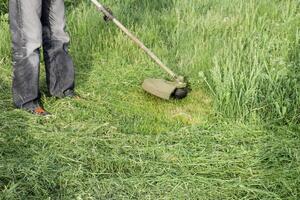 Anwendung Trimmer. Mähen Grün Gras mit ein Angeln Linie Trimmer foto